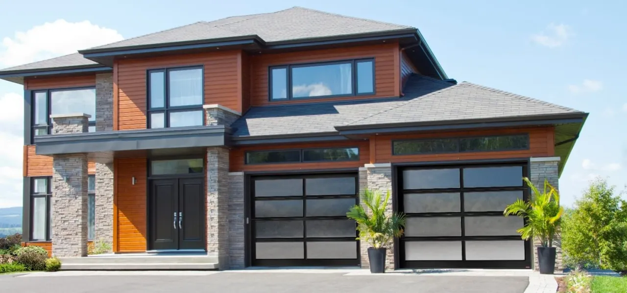 Maison en pierres de couleur gris-beige, avec vinyle orange brulé, agencés avec 2 portes de garage vitrées California avec verre Sablé blanc.
